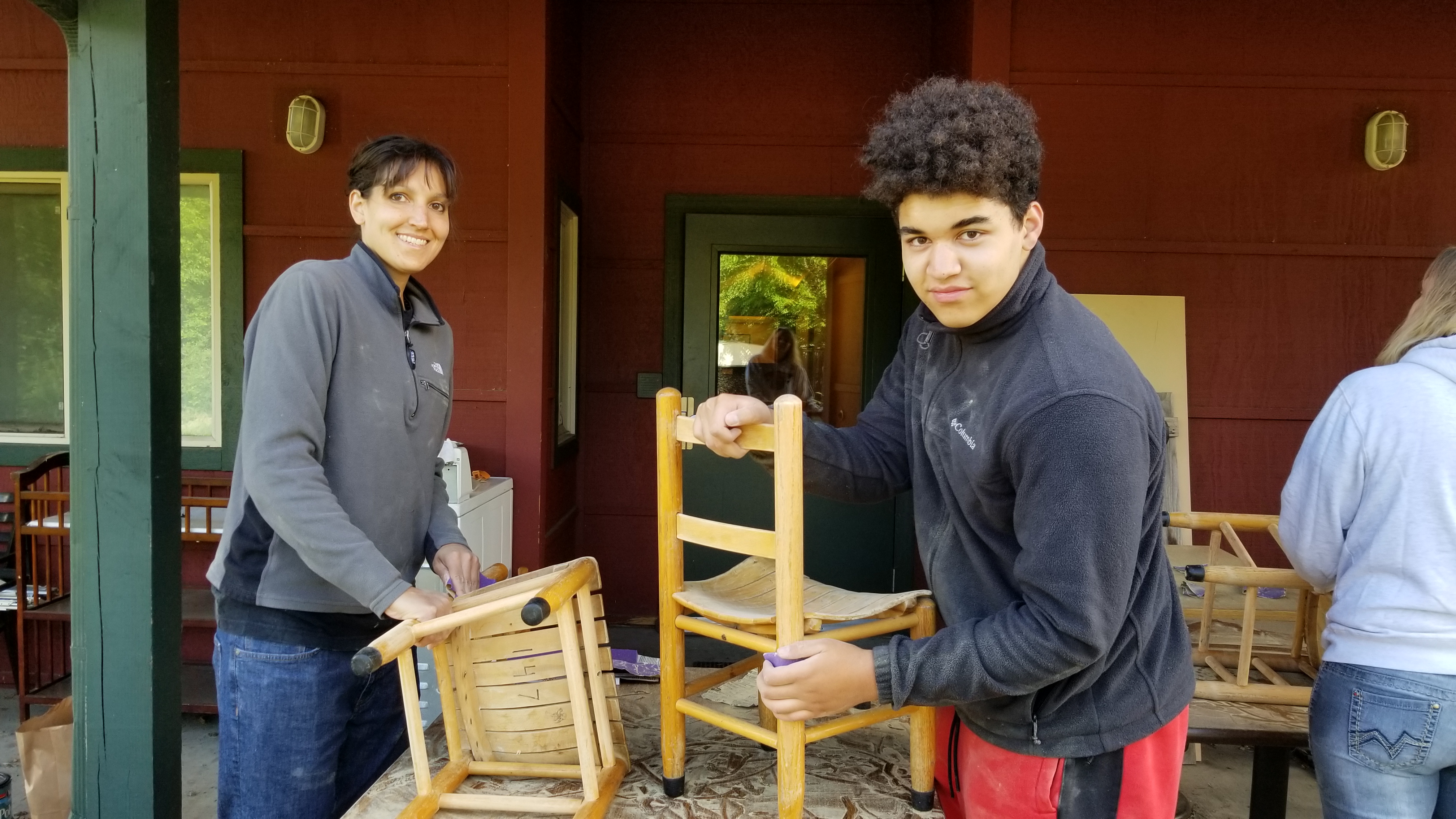 Two Day of Service Volunteers sanding child size wooden chairs.